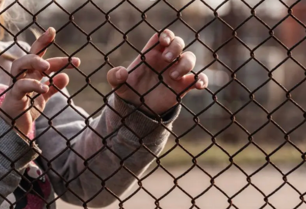 Child’s hands holding onto a metal mesh fence